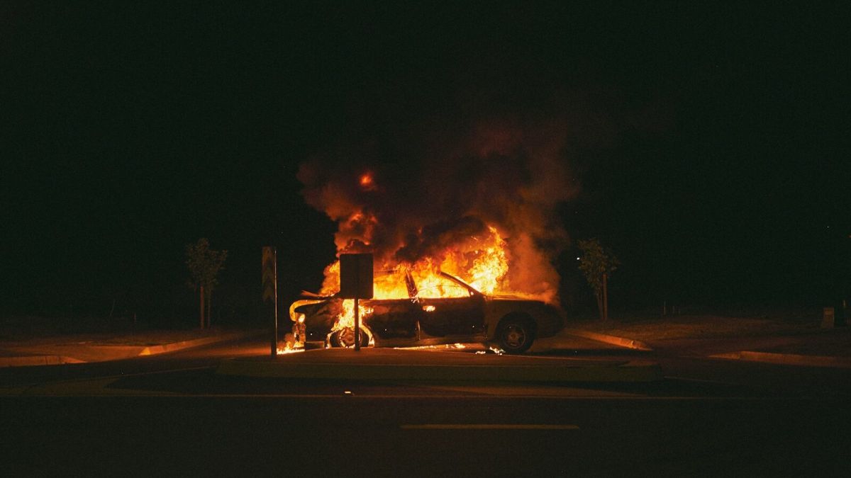 burning grey sedan near trees and signboard at night