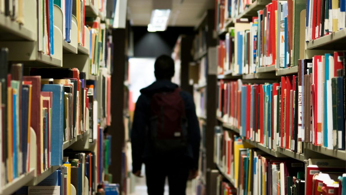 man with backpack beside a books