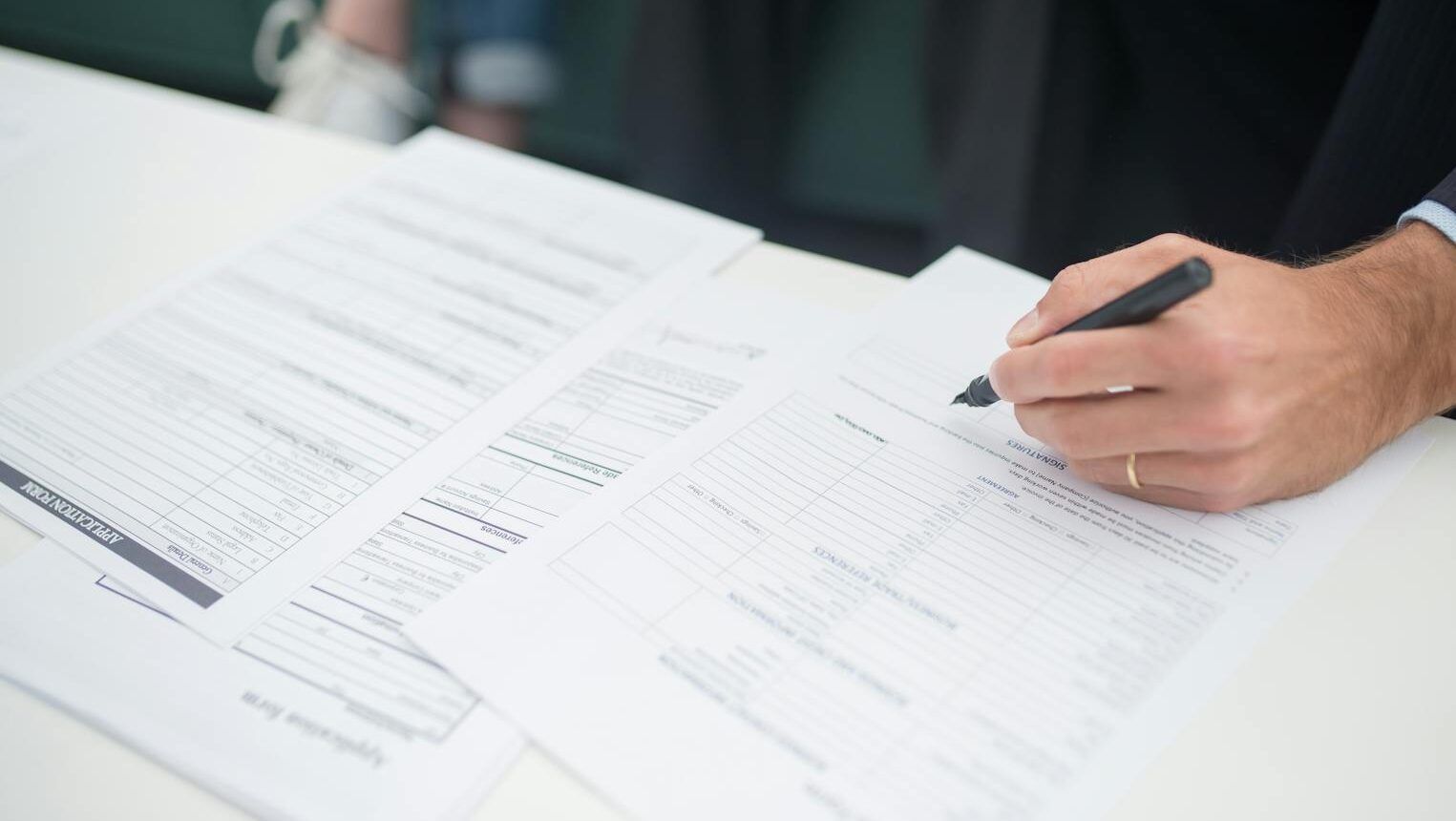 Close-up of a hand signing insurance documents in an office setting.