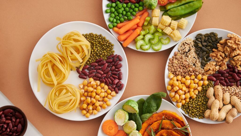 A vibrant mix of legumes, vegetables, nuts, and pasta arranged on white plates showcasing a balanced, healthy diet.