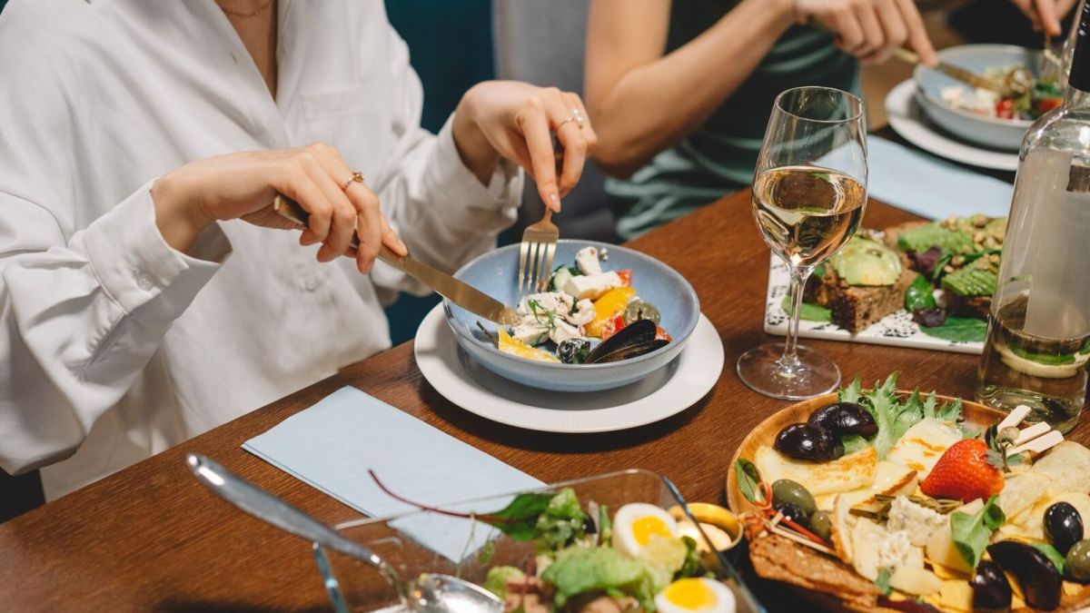 Elegant dining setting featuring fresh salad, dishes, and white wine, capturing a social gathering ambiance.